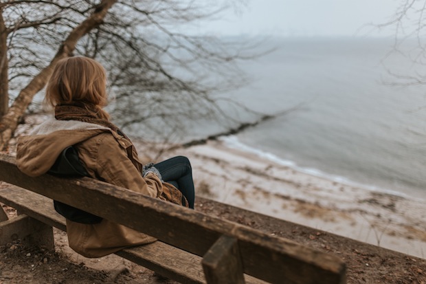 Frau auf Bank sitzend schaut depressiv auf See