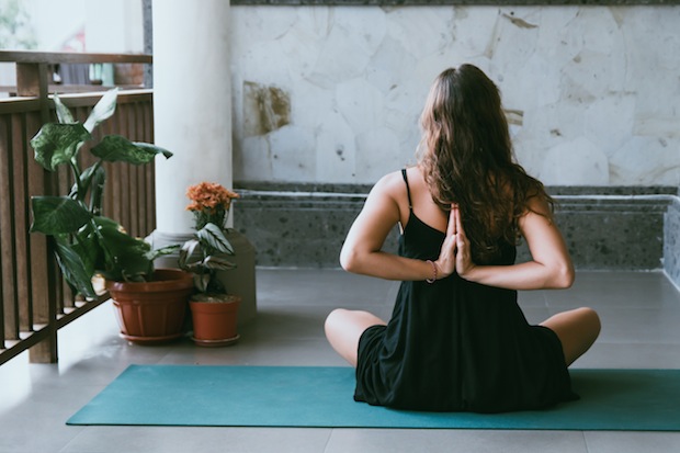 Frau sitzt auf Yogamatte mit gefalteten Händen im Rücken als Yogatherapie bei Depression